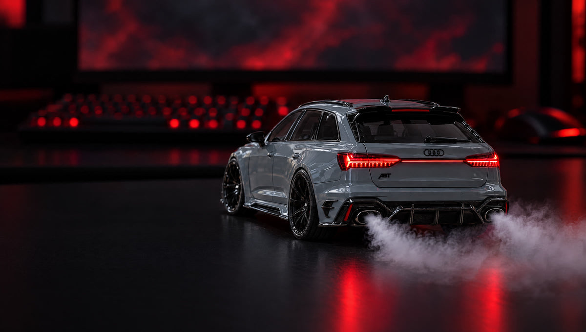 Nardograuer Audi RS6 ABT als Motor Mist-Modellauto mit Nebel aus dem Auspuff, auf einem Schreibtisch im Gaming-Setup bei Nacht